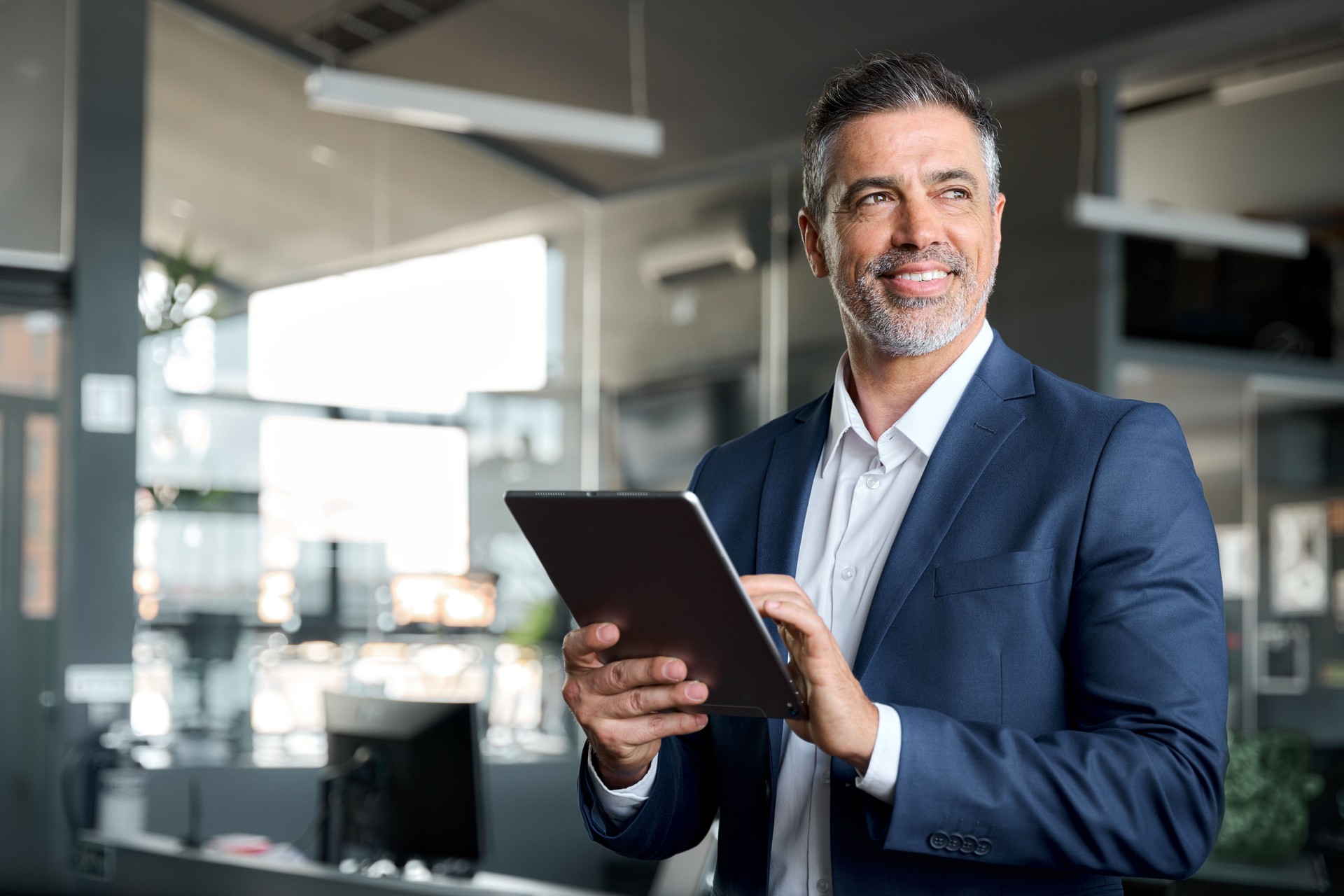 Felice dirigente maturo dell'uomo d'affari che indossa l'abito in ufficio usando il tablet.